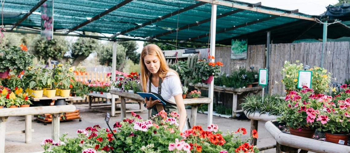 Female worker in a garden center with a tablet caring for flowers