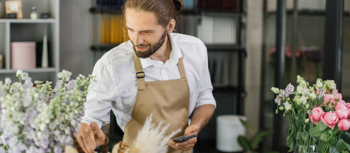 Male florist in flower shop. Floral design studio, making decorations and arrangements.